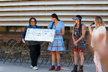 Two women hold up a big check while two other women look on