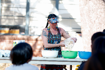 A woman in a patterned dress and visor pours popcorn into a green bowl
