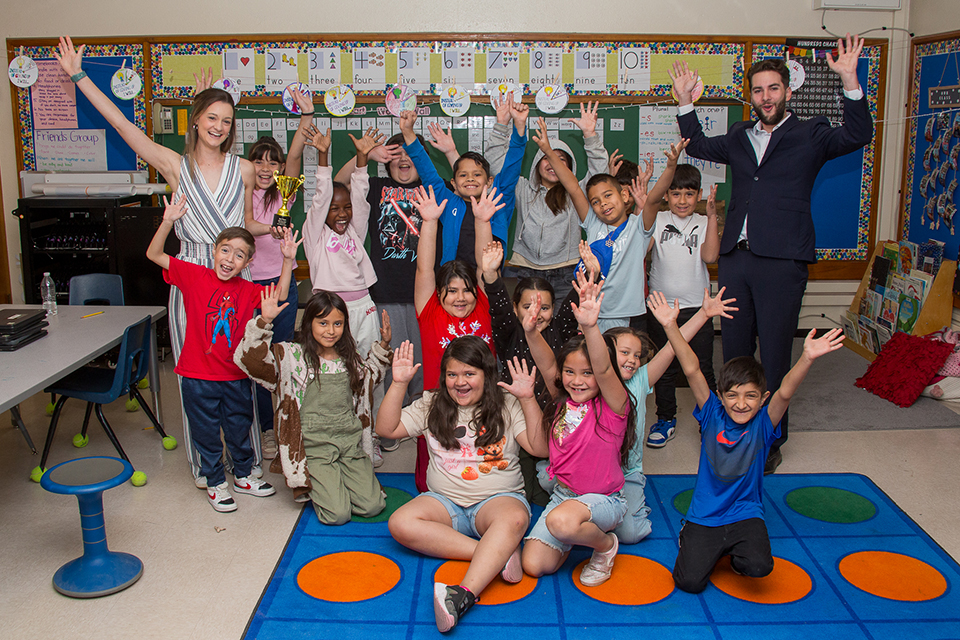 Students hold up their arms excitedly for a group photo