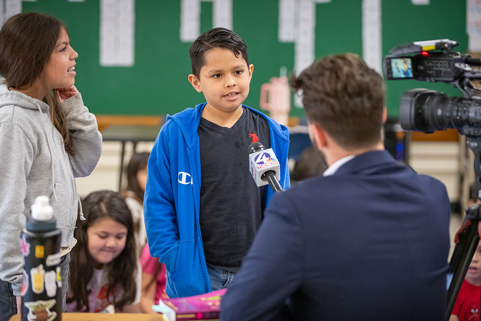 A boy talks into a news microphone