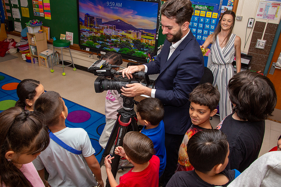 Students gather around as a news reporter shows them his camera