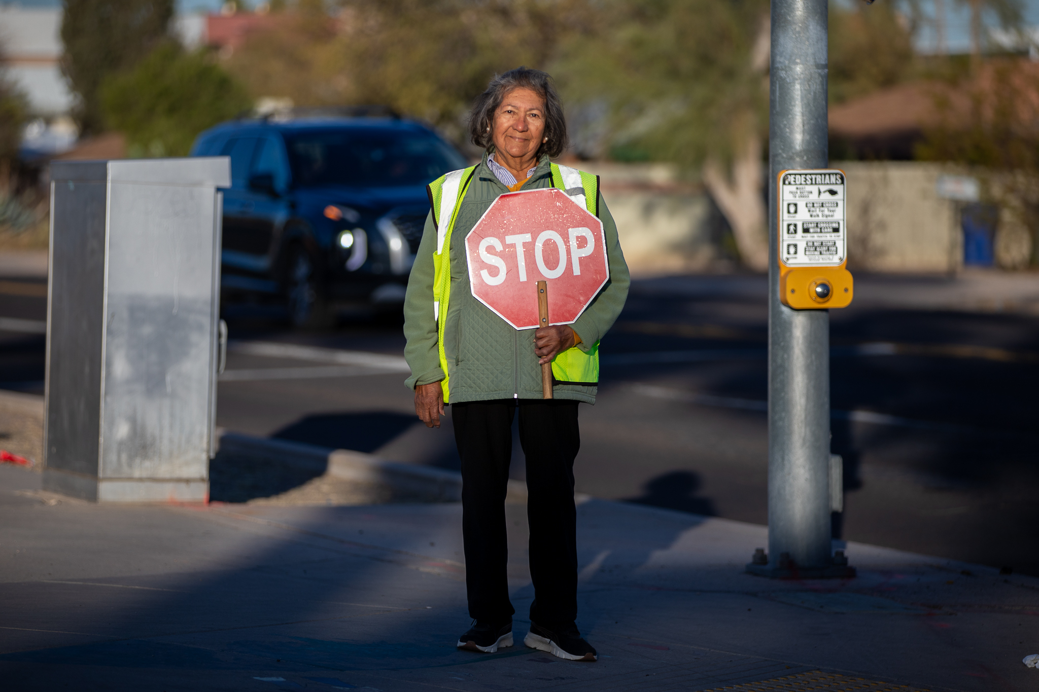 A woman in a yellow safety vest holds a stop sign on a street corner