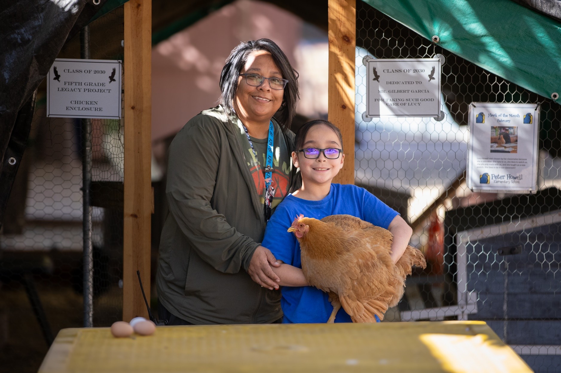 A woman in glasses stands next to her daughter in glasses who's holding a chicken