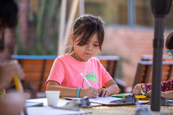 A little girl in a pink shirt colors with a marker