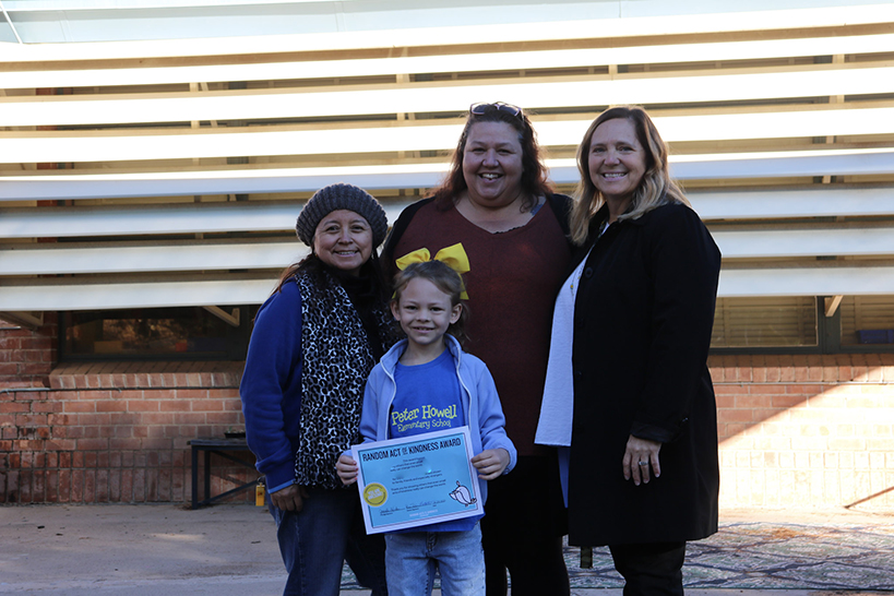 Three women smile, surrounding a little girl holding an award certificate
